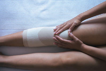 Close up of hand woman using elastic bandage with legs having knee or leg pain,Female feeling exhausted and painfulの写真素材
