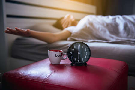 Blur of asian woman wake up stretch oneself and yawn on the bedroom with  black alarm clock 