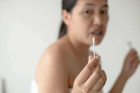 Woman cleaning her ears with cotton bud in bedroom,Female using cotton stickの写真素材