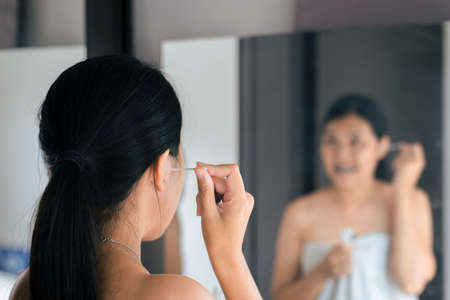 Woman cleaning her ears with cotton bud in bedroom,Female using cotton stick