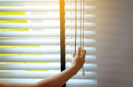 Hands woman opening blinds window in living room to get sunlightの写真素材