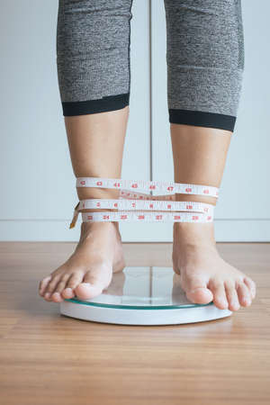 Woman foot standing on electronic weigh scales with tape measure legs windedの写真素材