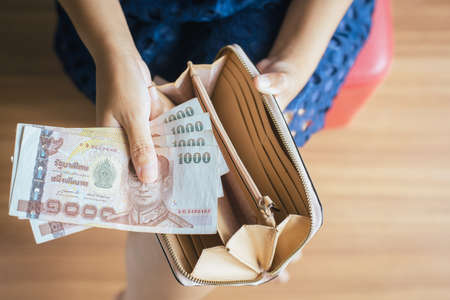 Hands woman counting Thai baht banknote bills into walletの写真素材