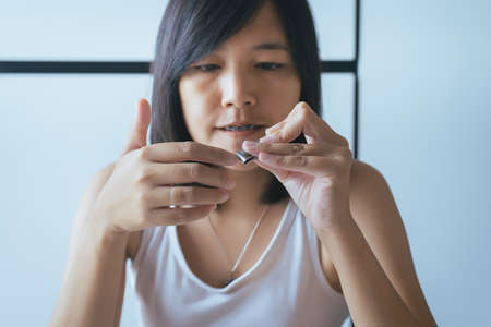 Asian woman cutting nails with using nail clipper in bedroom