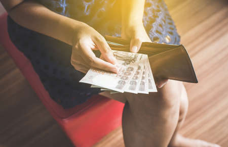 Hands woman counting Thai baht banknote bills into wallet