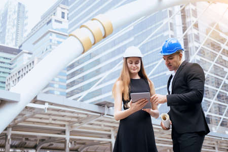 Male and female industrial engineers holding a tablet and blueprints working and discussing on...