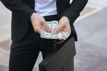 Business man in suit holding money US dollar bills and counting