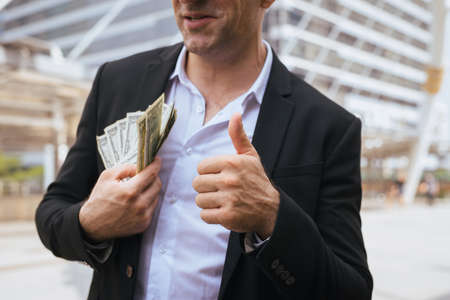 Business man in suit holding money US dollar bills and thumbs up
