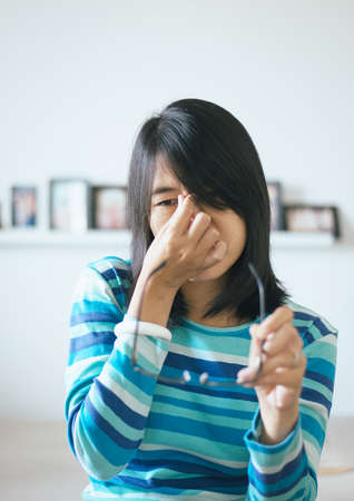 Woman suffering from eye pain hand holding eyeglasses and rubs her nose eyes out of fatigueの写真素材