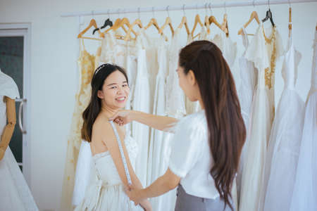 Asian bride trying on wedding dress,Woman designer making adjustment in fashion studio,Happy and smilingの写真素材