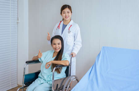 Patient woman is sitting in a wheelchair with doctor standing behind smiling and thumbs upの写真素材