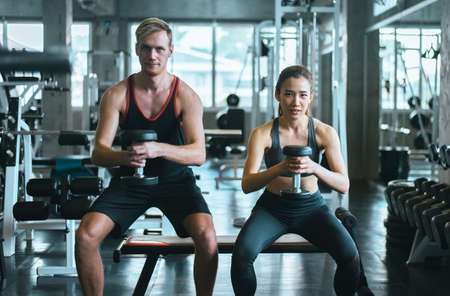 Sporty couple man and woman exercise with dumbbells or does the exercises at gym