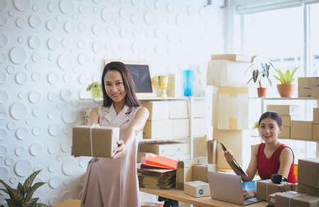 Happy asian business woman owner holding parcel and working together,Female smiling start up entrepreneur SME online at home officeの写真素材