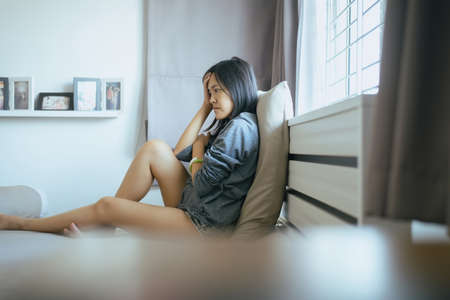 Asian women sitting on bedroom at home,Female feeling headache and confused problem in personal life,Contraception and unexpected pregnancy conceptの写真素材