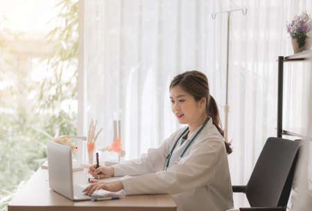 Doctor asian women sitting and working on desk using laptop and writing note at hospitalの写真素材