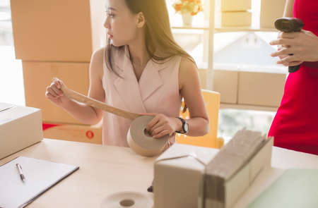Asian woman owner using scotch tape packaging product and working at home office,Start upentrepreneur SME online small businessの写真素材