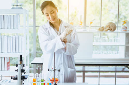 Scientist beautiful women putting rubber gloves on hands for working medical chemicals sample on microscope at laboratoryの写真素材