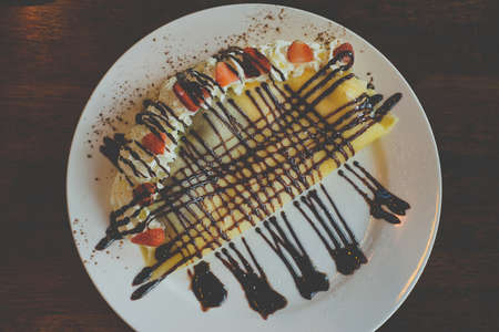 Pancakes with bananas and chocolate caramel sauce,Topping with whip cream and strawberry on table,Top viewの写真素材