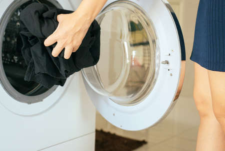 Hands woman getting in dirty clothes into washing machine doing laundry at homeの写真素材