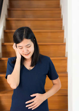 Asian beautiful pregnant woman standing with hand holding her belly at home,Happy mood and positive...