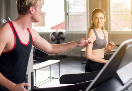 Happy and smiling couple young teen running on treadmills doing cardio training in a gym...