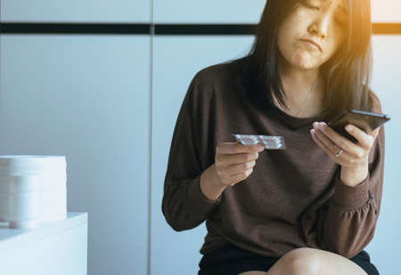 Asian woman using cell phone searching internet and reading drug or pill label and prescription medications,Health care concept,Close up and selective focusの写真素材