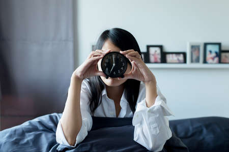 Young lazy woman in white shirt hates getting stressed waking up early 7 o'clock in the morningの写真素材