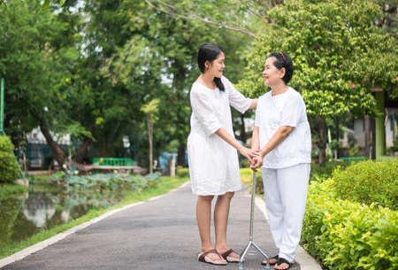 Elderly asian woman walking to do physical with stick at park,Daughter take care and supportの写真素材