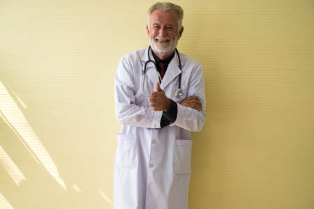 Portrait of senior doctor standing and showing thumb up at hospital,Happy and smiling positive thinking attitude,Copy space for textの写真素材
