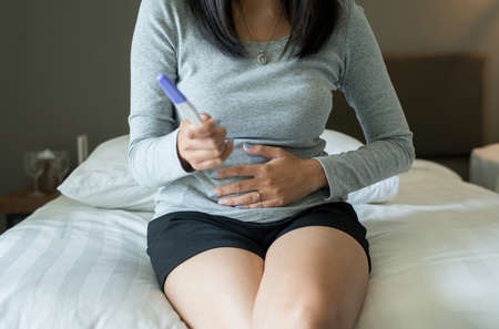 Asian woman hand touching her belly after testing pregnancy test in her bedroom,Close upの写真素材