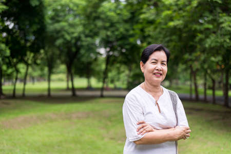 Portrait of elderly asian woman standing and cross arms at park,Happy and smiling,Positive attitude thinkingの写真素材