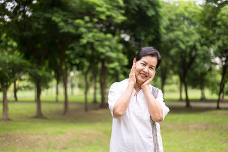 Portrait of elderly asian women standing and hand touching her cheek at park,Happy and smiling,Positive attitude thinkingの写真素材