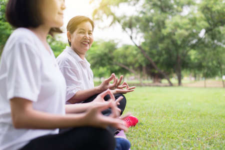 Elderly asian woman practicing yoga sitting at park in the morning,Happy and smiling,Positive...