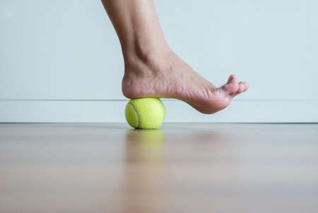 Woman massage with tennis ball to her foot in bedroomの写真素材