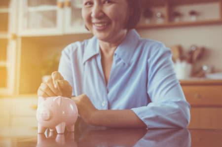 Senior asian hands putting coin to piggy bank for retirement, Happy and smiling, Saving money conceptの写真素材