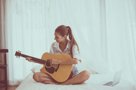 Beautiful woman hands playing guitar on bedroom in the morning, Relaxing timeの写真素材
