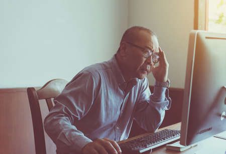 Asian senior man serious working and using computer at home in the morningの写真素材