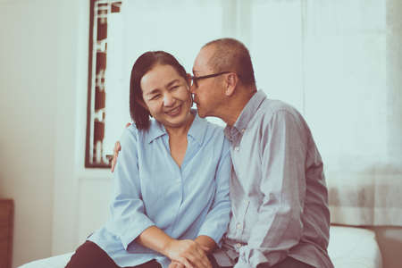 Happy couple senior asian kiss to cheek togeter on bed at home