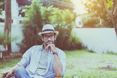Caucasian man wearing hat and glasses and sitting on chair at park,Happy and smiling,Relaxing timeの写真素材
