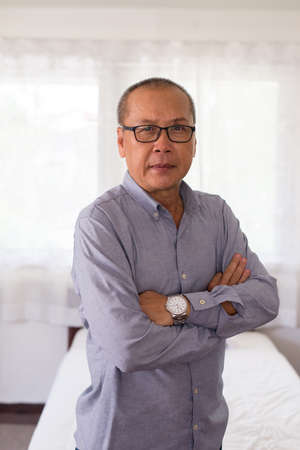 Portrait of elderly asian man standing cross arms and looking camera indoorの写真素材