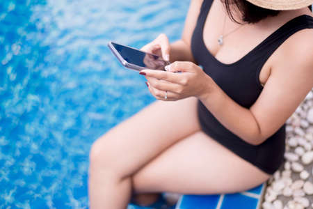 Beautiful asian woman using mobile phone at swimming pool,Happy and smiling,Relax time,Summer travel conceptの写真素材