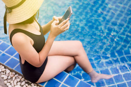 Beautiful asian woman using mobile phone at swimming pool,Happy and smiling,Relax time,Summer travel conceptの写真素材
