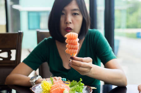 Hands woman holding fresh salmon sashimi in restaurantの写真素材