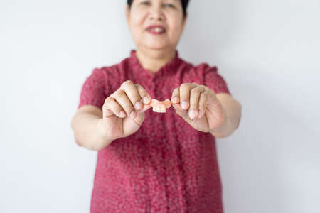 Senior asian woman is holding dentures in hands. Dental prosthesis,False teeth,Close upの写真素材