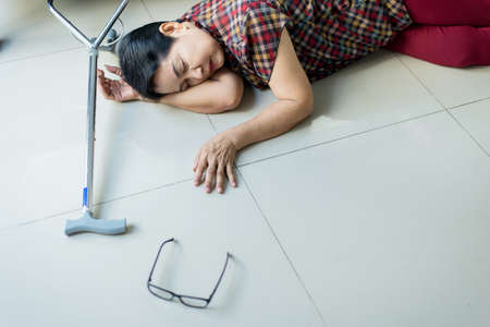 Senior asian woman suffering with faint lying on floor after falling down at homeの写真素材