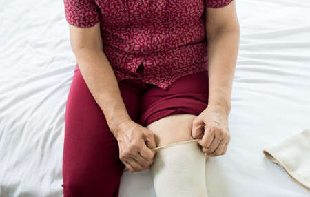 Senior asian woman using elastic bandage with leg,Female putting bandage on her injured kneeの写真素材