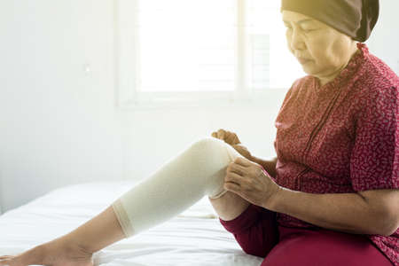 Elderly asian woman using elastic bandage with leg,Female putting bandage on her injured kneeの写真素材