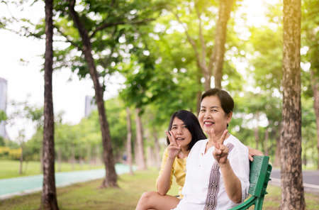 Portrait of middle aged asian female with daughter showing 2 finger together at outdoor,Happy and smiling,Positive thinking,Take care and support conceptの写真素材