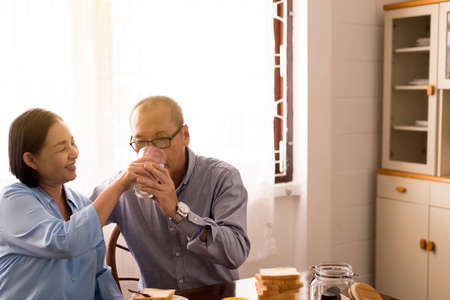 Retirement senior lifestyle living concept, Asian elderly couple drinking milk for breakfast togetherの写真素材