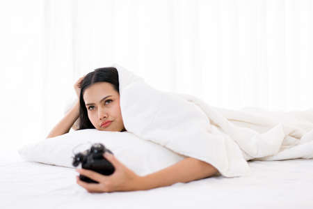 Bored Asian woman hates getting stressed waking up early morning on bed, Alarm clock